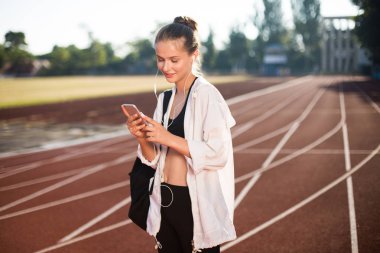 Gülümseyen kız mutlu istimal cellphone harcama zaman Stadyumu treadmill omuz sırt çantası ile kulaklık