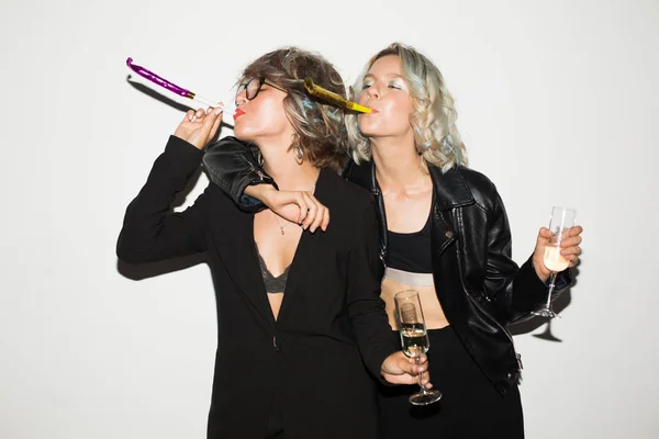 两个美丽的女孩在黑色夹克拿着香槟杯愉快地使用喧闹在白色背景 — 图库照片