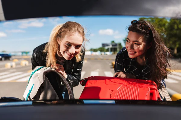Дві Веселі Дівчата Щасливо Складають Валізи Разом Багажник Чорного Автомобіля — стокове фото