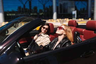 Güzel kız mutlu cabriolet ile gülümseyen arkadaş şehir sokaklarında açık araba güneş gözlüğü