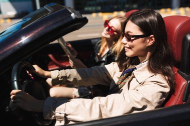 Gülümseyen kız mutlu cabriolet ile arkadaş şehir sokaklarında açık araba güneş gözlüğü