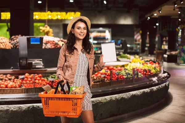 Joven Dama Sonriente Cesta Celebración Del Sombrero Lleno Productos Mirando —  Fotos de Stock