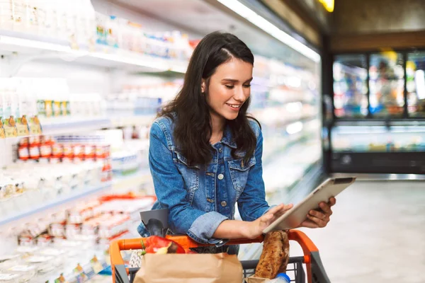 Усміхнена Дівчина Джинсовій Куртці Візком Повним Продуктів Щасливо Використовуючи Планшет — стокове фото