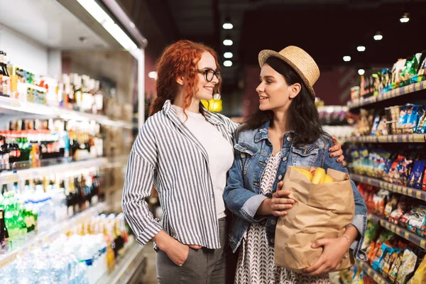 楽しく見て他の近代的なスーパー マーケットで時間を費やして製品の完全食料品紙袋と陽気な女の子 — ストック写真