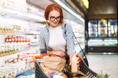 Güzel kız gözlük ve alışveriş sepeti ürünleri modern süpermarket süt bölümünde tam ile çizgili gömlek