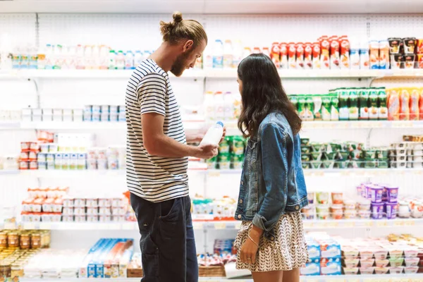 若い美しいカップル近代的なスーパー マーケットの酪農部で一緒に思慮深く選択ミルク — ストック写真