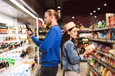Genç güzel çift ayakta sırt sırta düşünceli modern süpermarkette vakit ürünler seçme 
