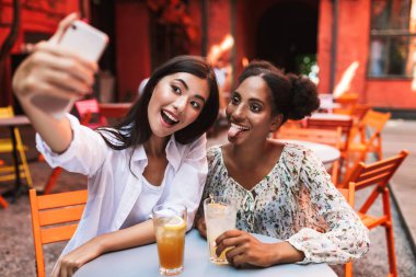 Neşeli kızlar Sevimli fotoğraflar mutlulukla birlikte kafe rahat avluda vakit cep telefonu alarak kokteyller ile masada oturan 