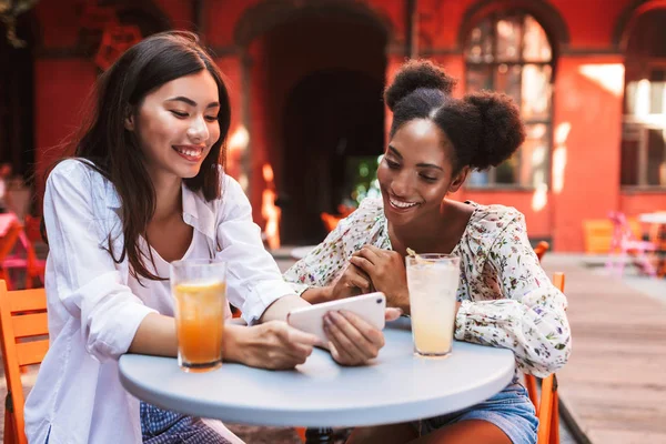 Due Belle Signore Felicemente Utilizzando Cellulare Insieme Bevande Vicino Tavolo — Foto Stock