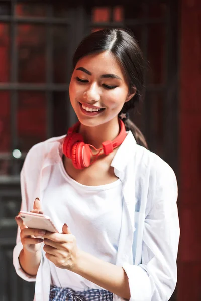 快乐的女孩在白色衬衣和红色耳机愉快地使用手机室外 — 图库照片