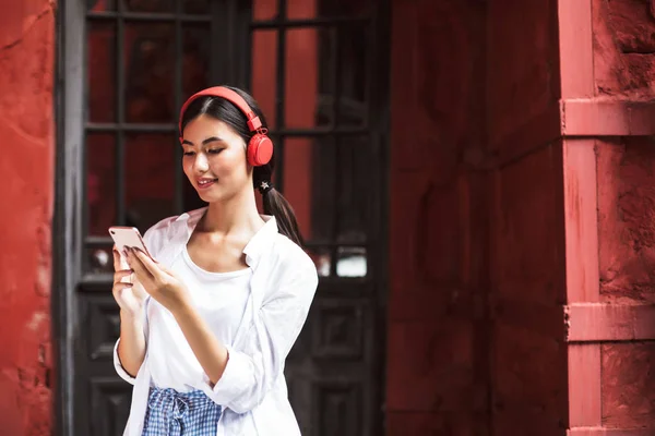Vakker Smilende Jente Hvit Skjorte Røde Hodetelefoner Som Bruker Mobiltelefon – stockfoto