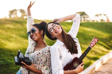 Küçük kamera sevinçle birlikte parkta vakit elinde gitar ve polaroid neşeli kızlar
