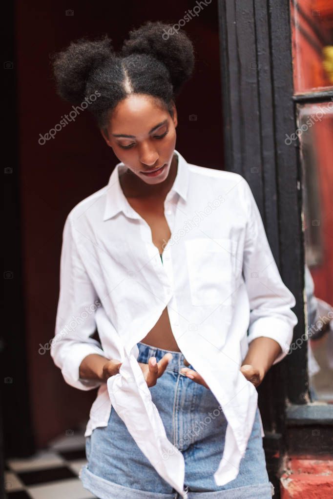 Beautiful african girl with dark curly hair in white shirt and denim shorts thoughtfully closing eyes isolated