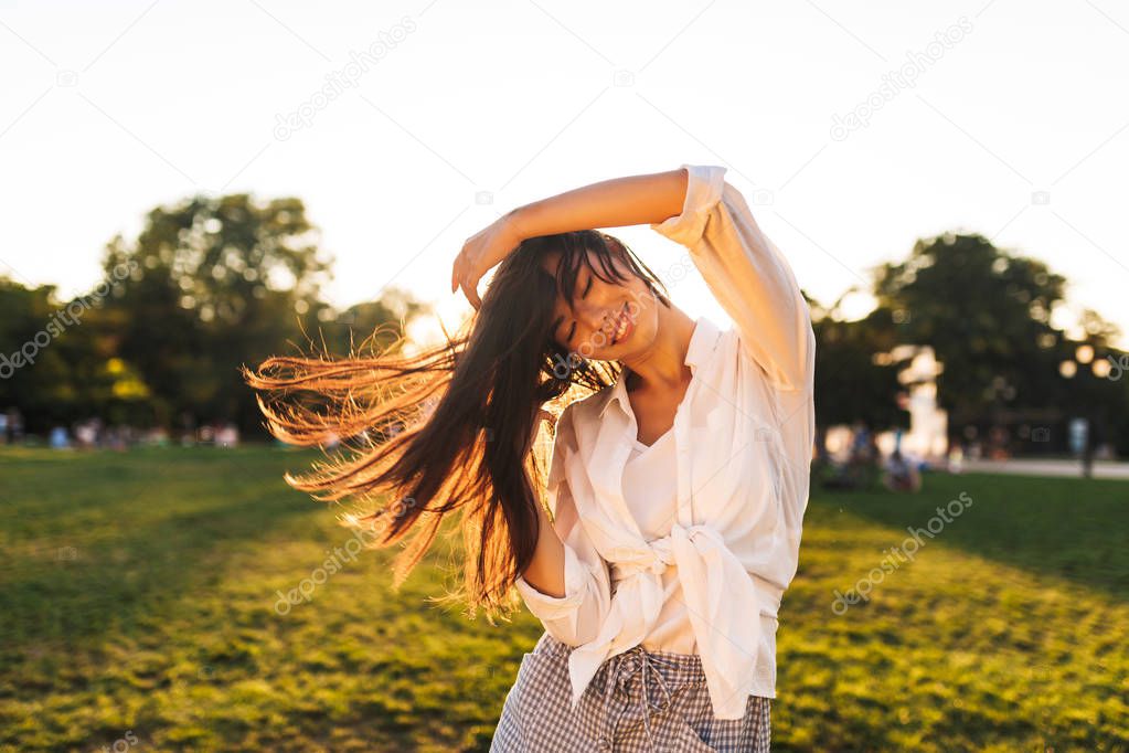 Beautiful smiling asian girl in white shirt happily dancing spending time in city park