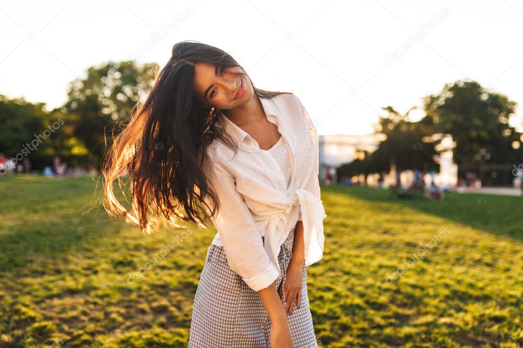 Beautiful smiling asian girl in white shirt dreamily looking in camera dancing in city park