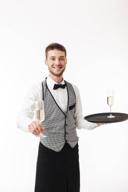 Sevinçle şampanya fotoğraf makinesinde beyaz arka plan üzerinde sunan tepsi tutarak üniformalı genç gülümseyen garson