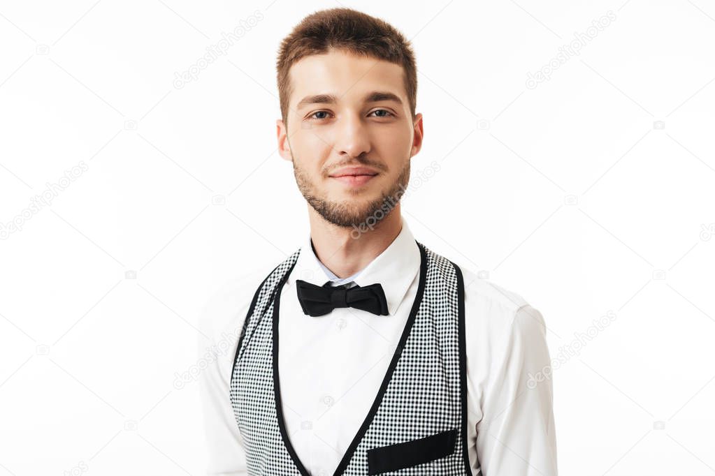 Portrait of young smiling waiter with beard in bow tie dreamily looking in camera over white background