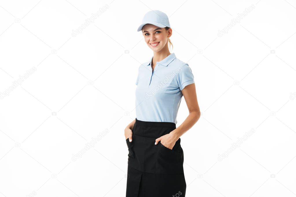 Cheerful girl in blue polo T-shirt and cap happily looking in camera holding hands in pockets over white background