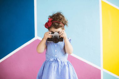 Şakacı kapsayan yüz retro kamera ve fotoğraf çekimi ile renkli arka plan üzerinde elbise siyah kıvırcık saçlı güzel kız