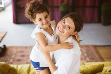 Beyaz gömlek ve mutlu bir şekilde kamera birlikte evde seyir sarılma küçük güzel kızı güzel genç anne