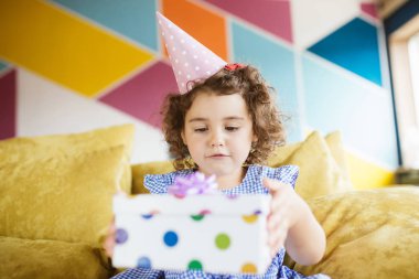 Sersem kanepe evde hediye kutusu açma Doğum günü kap karanlık kıvırcık saçlı kız şirin bebek