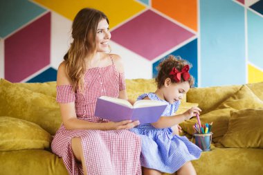 Küçük kızı mutlu keçeli kalemler evde kanepe ile boyama kitabı içinde birlikte çizim zaman harcama mavi elbiseli güzel annem 