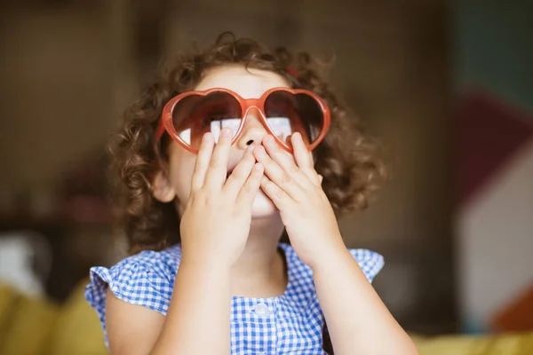 うっとりと自宅の手で口を覆っているハート サングラス ダーク巻き毛を持つかわいい女の子の肖像画 — ストック写真