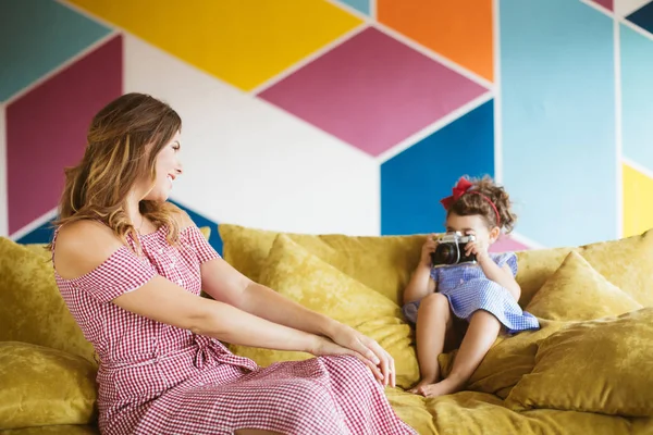 Şakacı güzel annesi evde kanepe retro kamera fotoğraf çekmek elbise siyah kıvırcık saçlı sevimli küçük kız