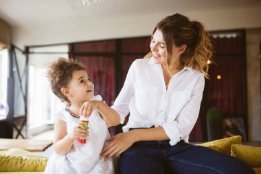 Beyaz gömlek ve mutlulukla birlikte vakit kabarcıklar evde üfleme elbiseli küçük şirin kızı Genç Anne