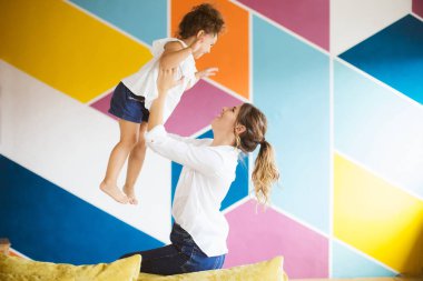 Beyaz gömlekli mutlulukla birlikte evde ile renkli duvar arka plan üzerinde vakit kadar küçük şirin kızı kaldırma oldukça genç anne