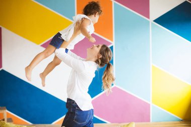 Genç Anne Beyaz gömlekli sevinçle birlikte evde ile renkli duvar arka plan üzerinde vakit kadar küçük güzel kızım kaldırma