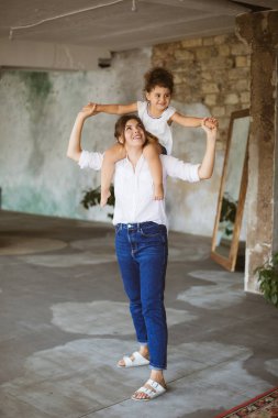 Genç Anne Bebek kızı sevinçle birlikte evde vakit omuzlarında tutan kot pantolon ve beyaz gömlek güzel