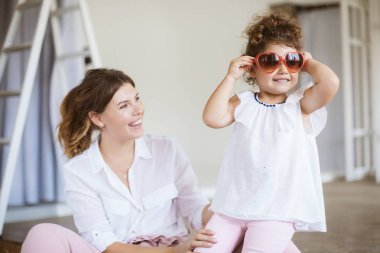 Mutlu bir şekilde seyir oldukça küçük kızı evde birlikte vakit yetişkin güneş gözlüğü takıyor neşeli Genç Anne