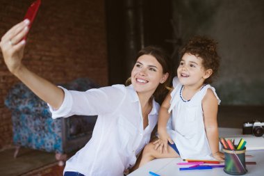 Güzel gülümseyen anne ve şirin bebek kızı mutlu rahat evde birlikte vakit cep telefonu üzerinde fotoğraf çekmek