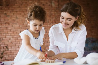 Beyaz gömlekli Genç Anne ve sevimli küçük kızı sersem Not Defteri'nde keçeli kalemler ile birlikte rahat ev, çizim elbiseli gülümseyen