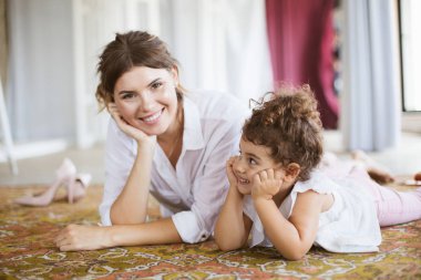 Güzel gülümseyen anne ve mutlulukla birlikte evde vakit halı üzerinde yalan beyaz gömlek içinde şirin küçük kız