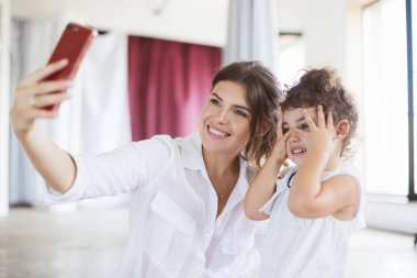 Çok gülümseyen anne ve sevimli küçük kız mutlu cep telefonu evde fotoğraf çekmek