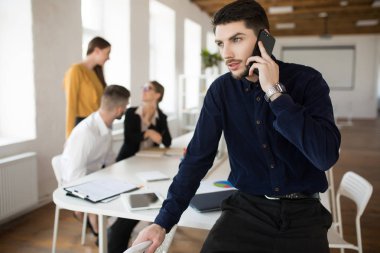 Sersem bir yana office cep telefonu arka plan meslektaşları ile konuşurken seyir karanlık gömlekli sakallı genç düşünceli iş adamı