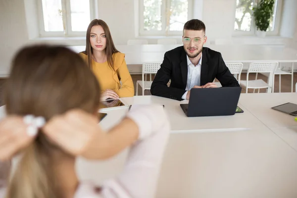 年轻的商人在眼镜与笔记本电脑和商业妇女附近若有所思地与申请人谈工作 年轻雇主在现代办公室里花费工作面试机会 — 图库照片