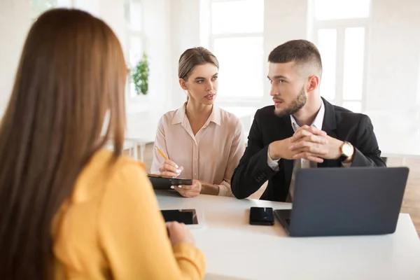 周到的业务人与笔记本电脑和商务妇女与铅笔和文件夹在手若有所思地咨询有关申请人 年轻雇主在现代办公室里花费工作面试机会 — 图库照片