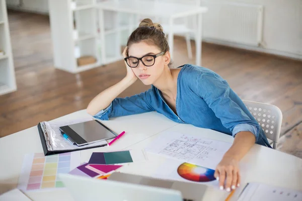 Tired girl in denim shirt and eyeglasses leaning on hand sleeping spending time in modern office