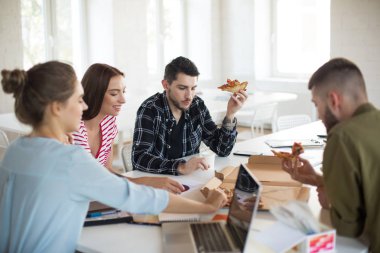 Grup Genç erkek ve kadınlar mutlu pizza yemek birlikte modern ofisinde. Yaratıcı gençlerin iş vakit