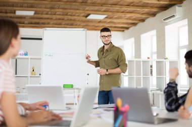 Gözlük ve gömlek ayakta sersem İşyerinde meslektaşları ile yeni proje tartışıyor kurulu yakınındaki genç gülümseyen adam. Grup birlikte modern ofisinde çalışan insan