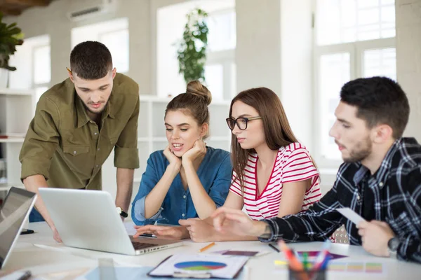 Grup düşünceli erkek ve kadınların iş vakit dizüstü bilgisayar ile. Gençler yaratıcı modern ofis birlikte tartışarak yeni proje