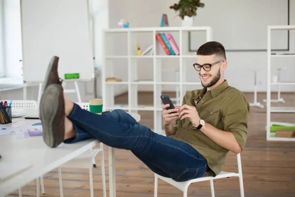 Joven Hombre Sonriente Con Anteojos Camisa Felizmente Usando Celular Sentado — Foto de Stock