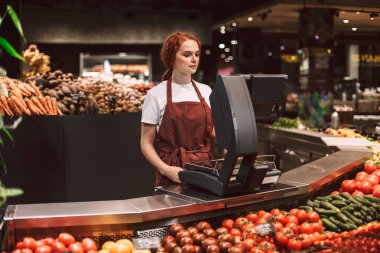 Önlük ayakta modern süpermarkette çalışma sebze ile tezgahın arkasındaki genç satıcı