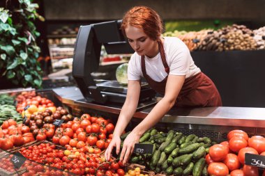 Önlük ayakta düşünceli modern süpermarkette çalışma sebze ile tezgahın arkasındaki genç satıcı