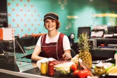 Mutlu bir şekilde modern süpermarkette çalışan kamera seyir üniformalı genç güzel kasiyer