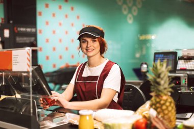 Sevinçle modern süpermarkette çalışan kamera seyir üniformalı genç kadın kasiyer
