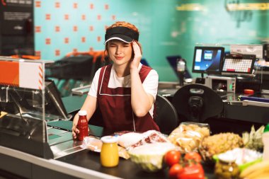 Modern süpermarkette çalışan baş ağrısı ile üniformalı genç kadın kasiyer
